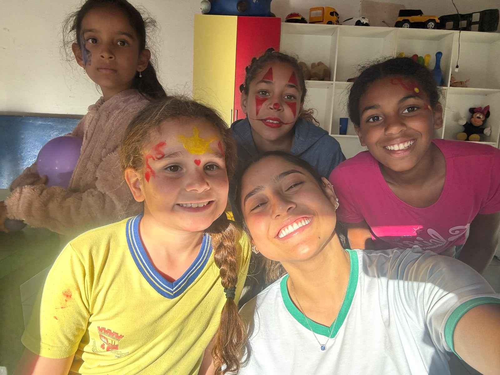 Crianças com pintura no rosto sorrindo ao lado de voluntária